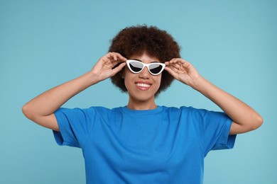 Happy young woman in stylish sunglasses on light blue background