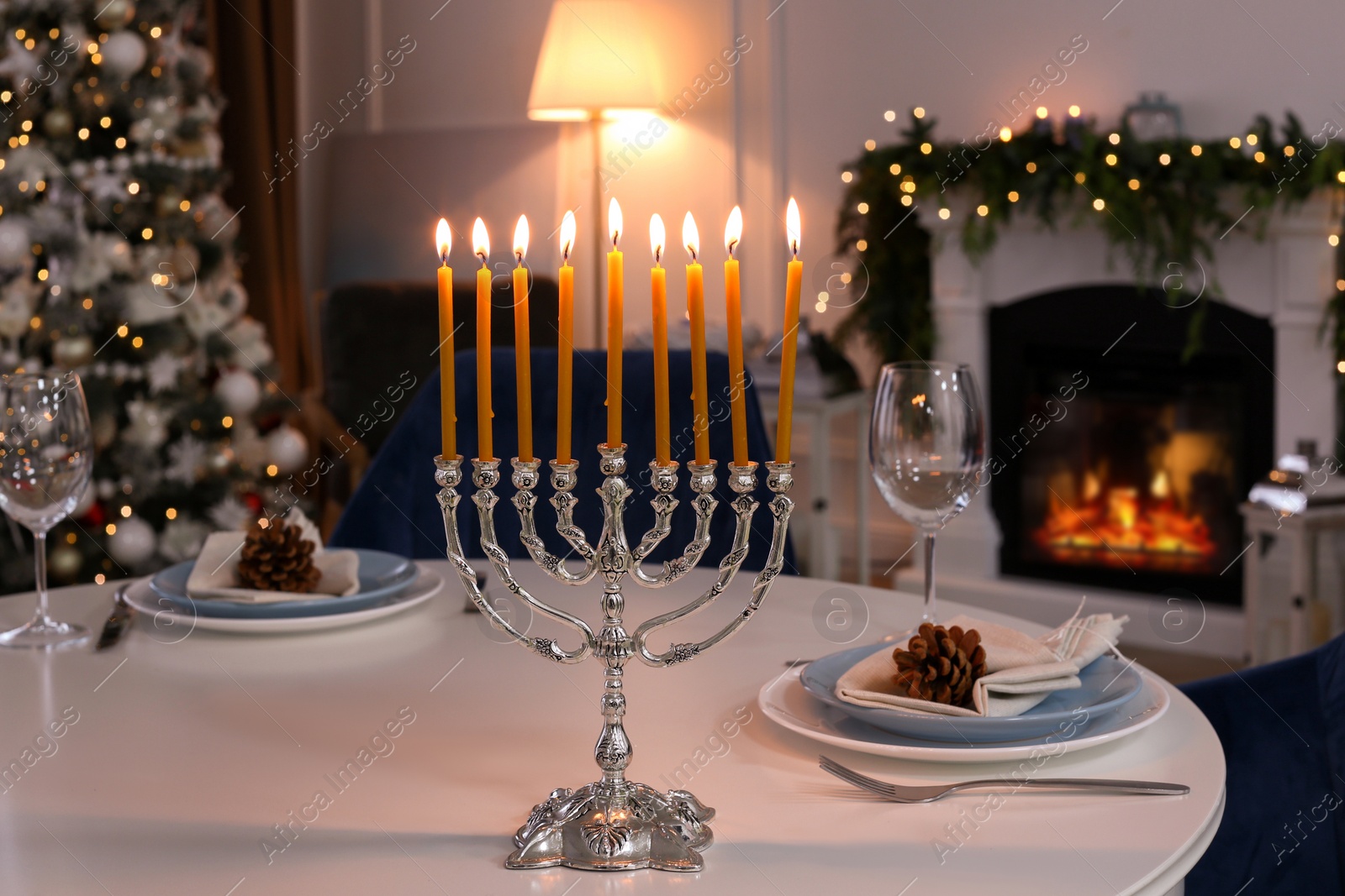 Photo of Silver menorah on white table in room with fireplace and Christmas decorations. Hanukkah symbol