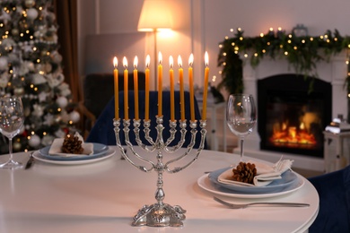 Photo of Silver menorah on white table in room with fireplace and Christmas decorations. Hanukkah symbol