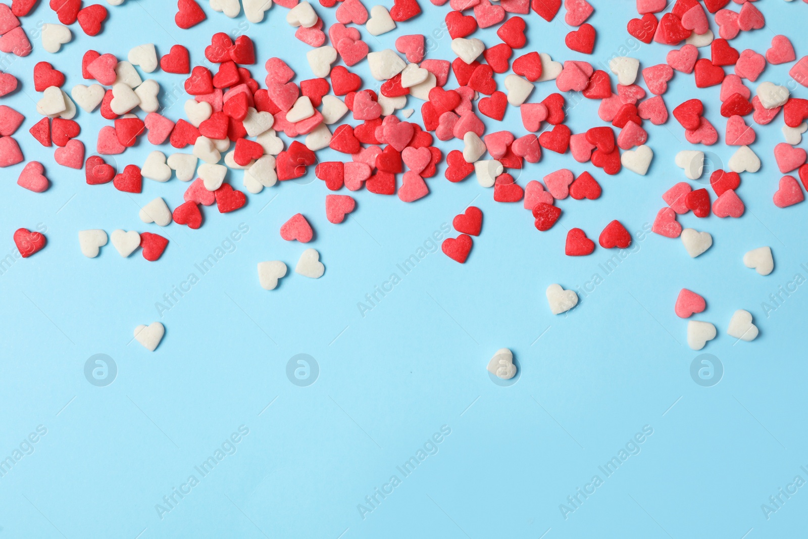 Photo of Bright heart shaped sprinkles on light blue background, flat lay. Space for text