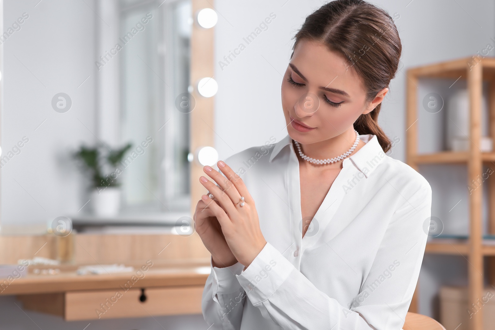 Photo of Young woman trying on elegant rings with pearls indoors, space for text