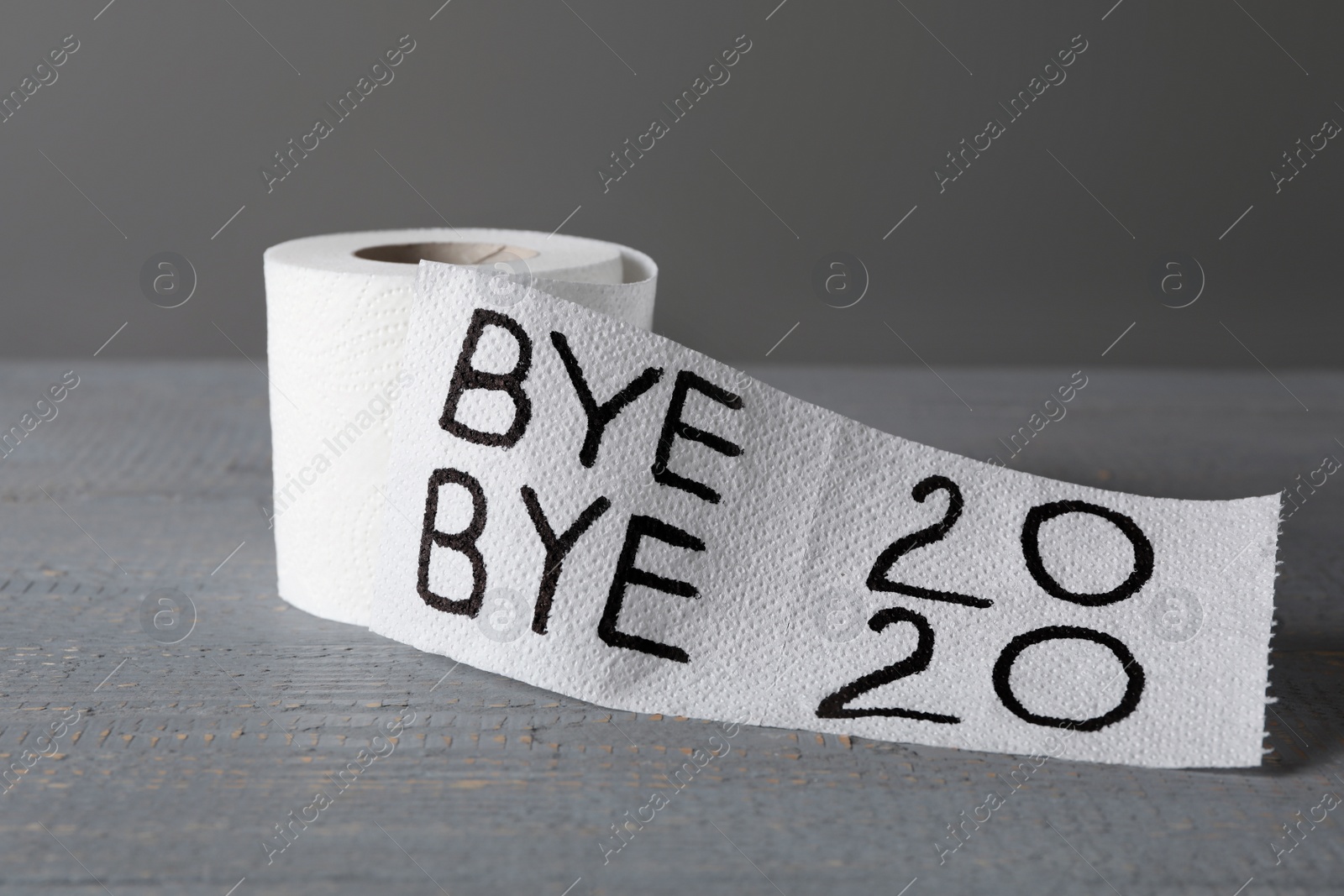 Photo of Toilet paper roll with text Bye Bye 2020 on light grey wooden background