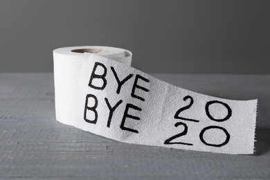 Photo of Toilet paper roll with text Bye Bye 2020 on light grey wooden background