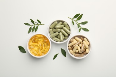 Photo of Different vitamin capsules in bowls and leaves on white background, flat lay