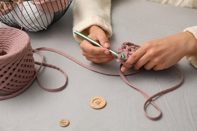 Photo of Woman crocheting with threads at grey table, closeup. Engaging hobby