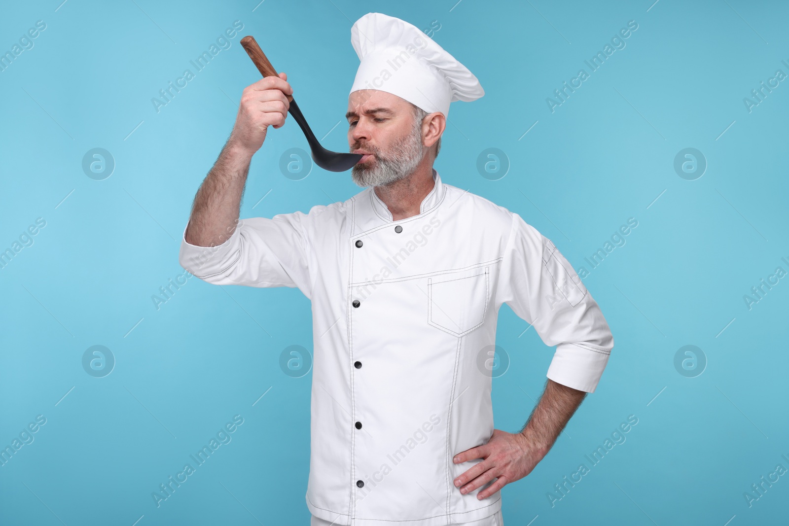 Photo of Chef in uniform tasting something on light blue background