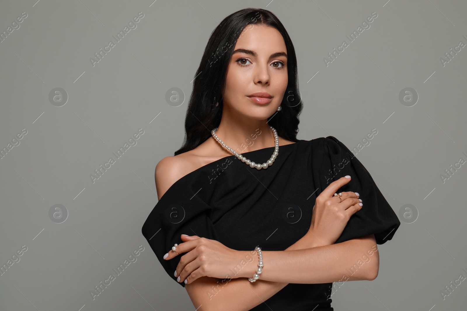 Photo of Young woman wearing elegant pearl jewelry on grey background, space for text