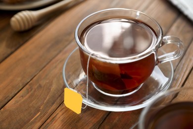 Photo of Tea bag in glass cup on wooden table, closeup