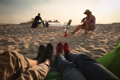 Photo of Friends resting on sandy coast, closeup. Beach camping