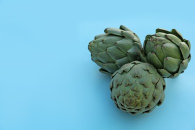 Photo of Whole fresh raw artichokes on light blue background. Space for text