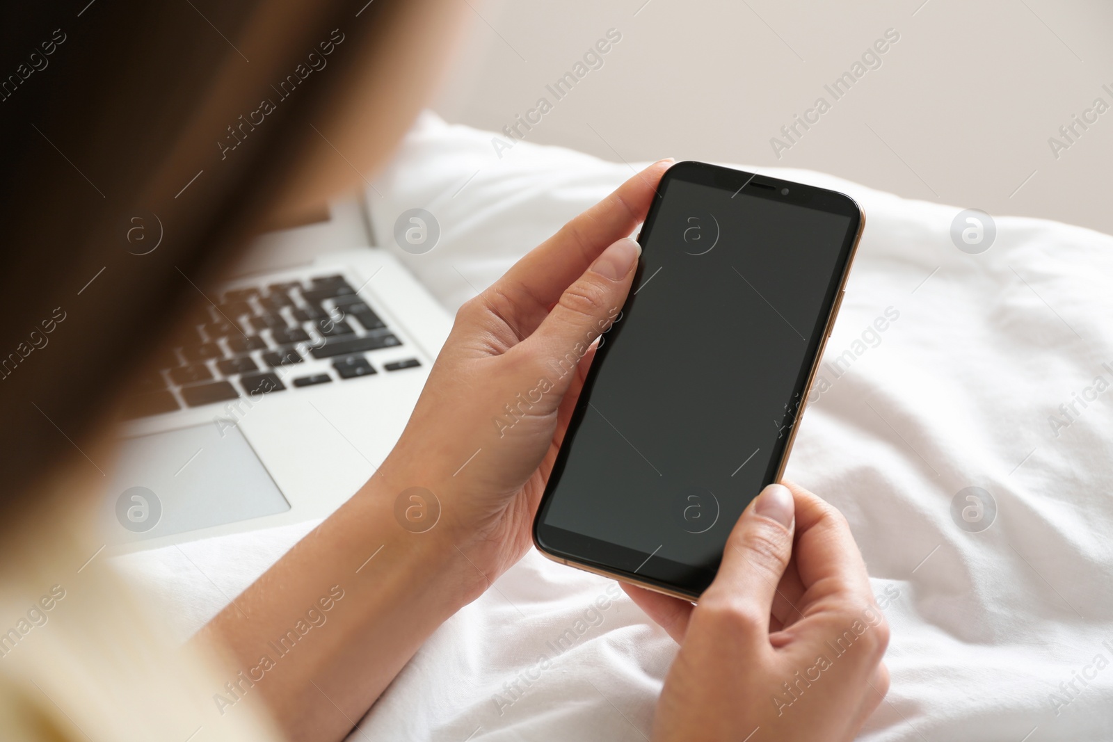 Photo of Young woman using modern smartphone on bed at home, closeup