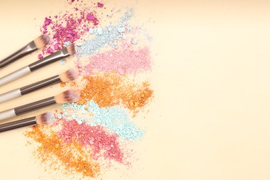 Photo of Makeup brushes and scattered eye shadows on beige background, flat lay. Space for text