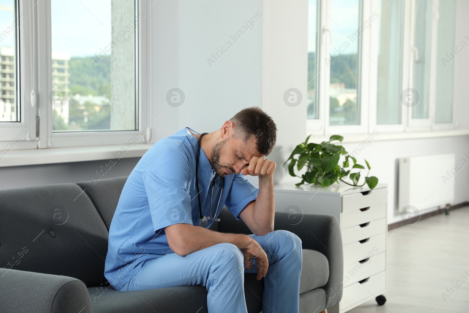 Photo of Exhausted doctor sitting on sofa in hospital