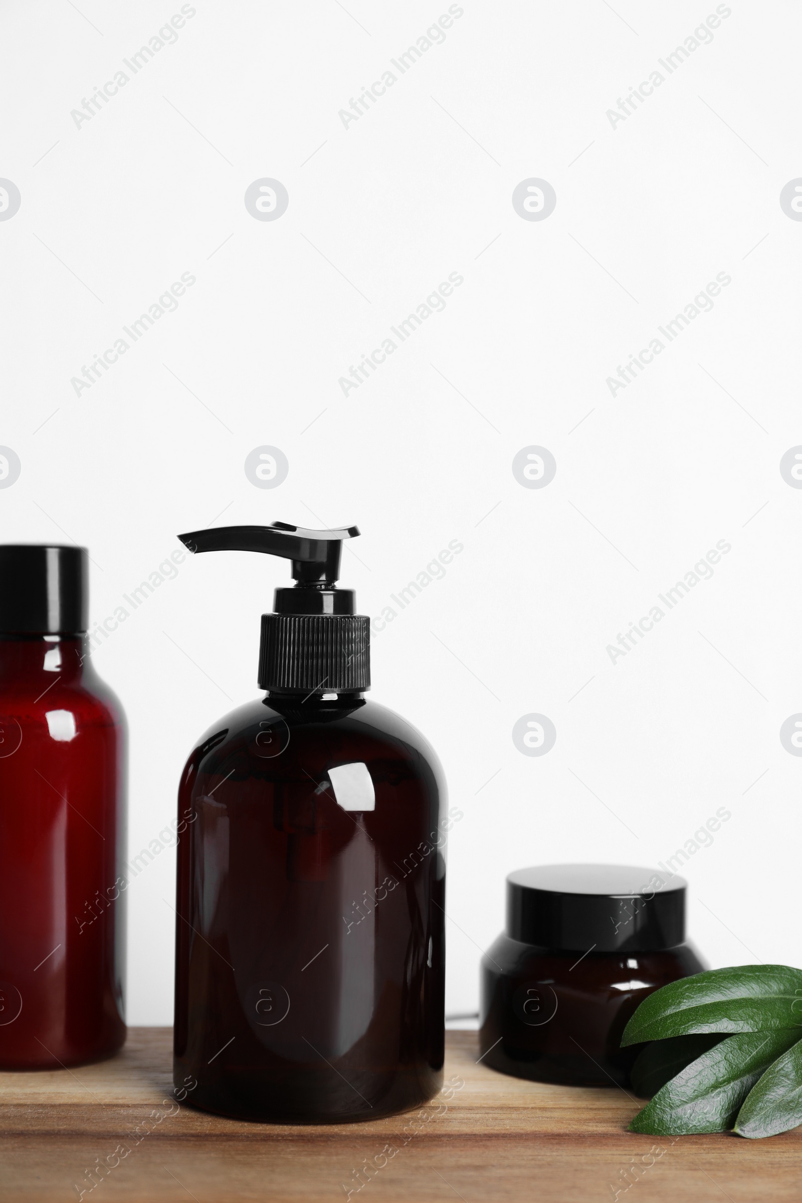 Photo of Different cosmetic products and leaves on wooden board
