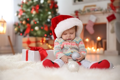 Cute little baby in Santa hat sitting on fur rug at home. Christmas celebration