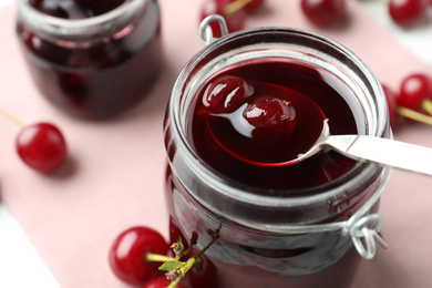 Jar of pickled cherries and fresh fruits on table, closeup