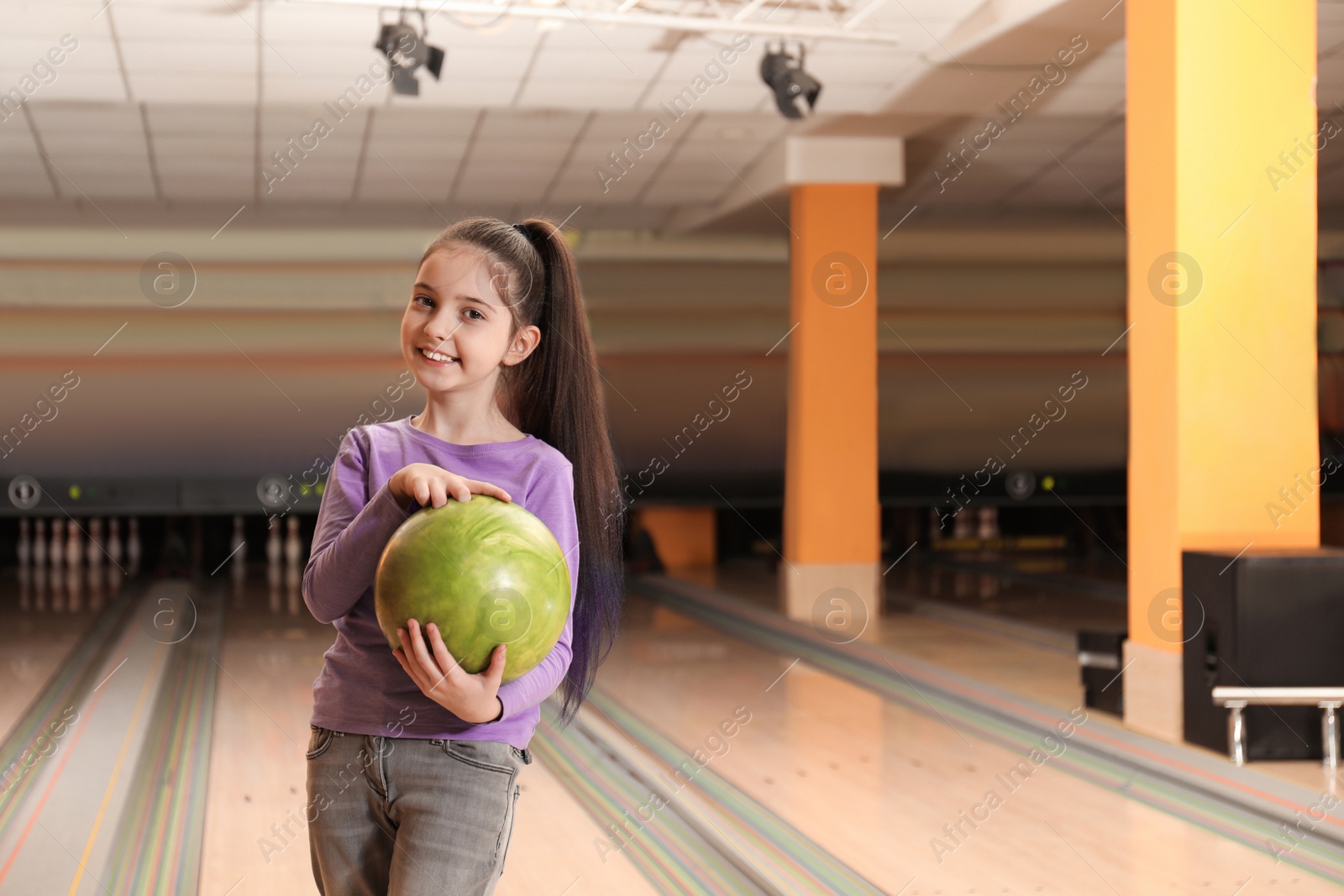 Photo of Little girl with ball in bowling club. Space for text