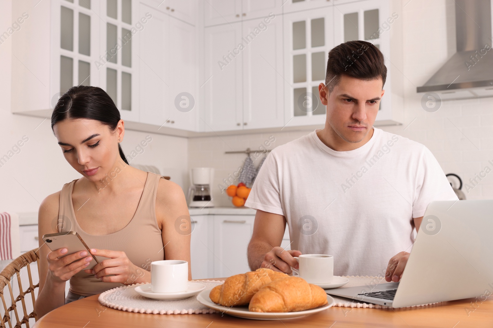 Photo of Internet addiction. Couple using gadgets at table in kitchen