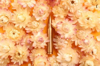 Photo of Bullet surrounded by beautiful flowers on orange background, flat lay