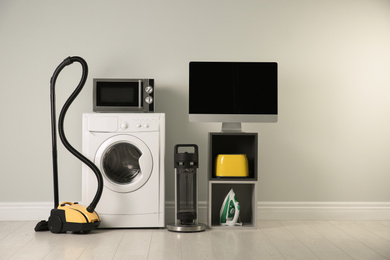 Photo of Modern vacuum cleaner and different household appliances near light wall indoors