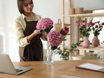 Photo of Florist with beautiful flowers at table in workshop