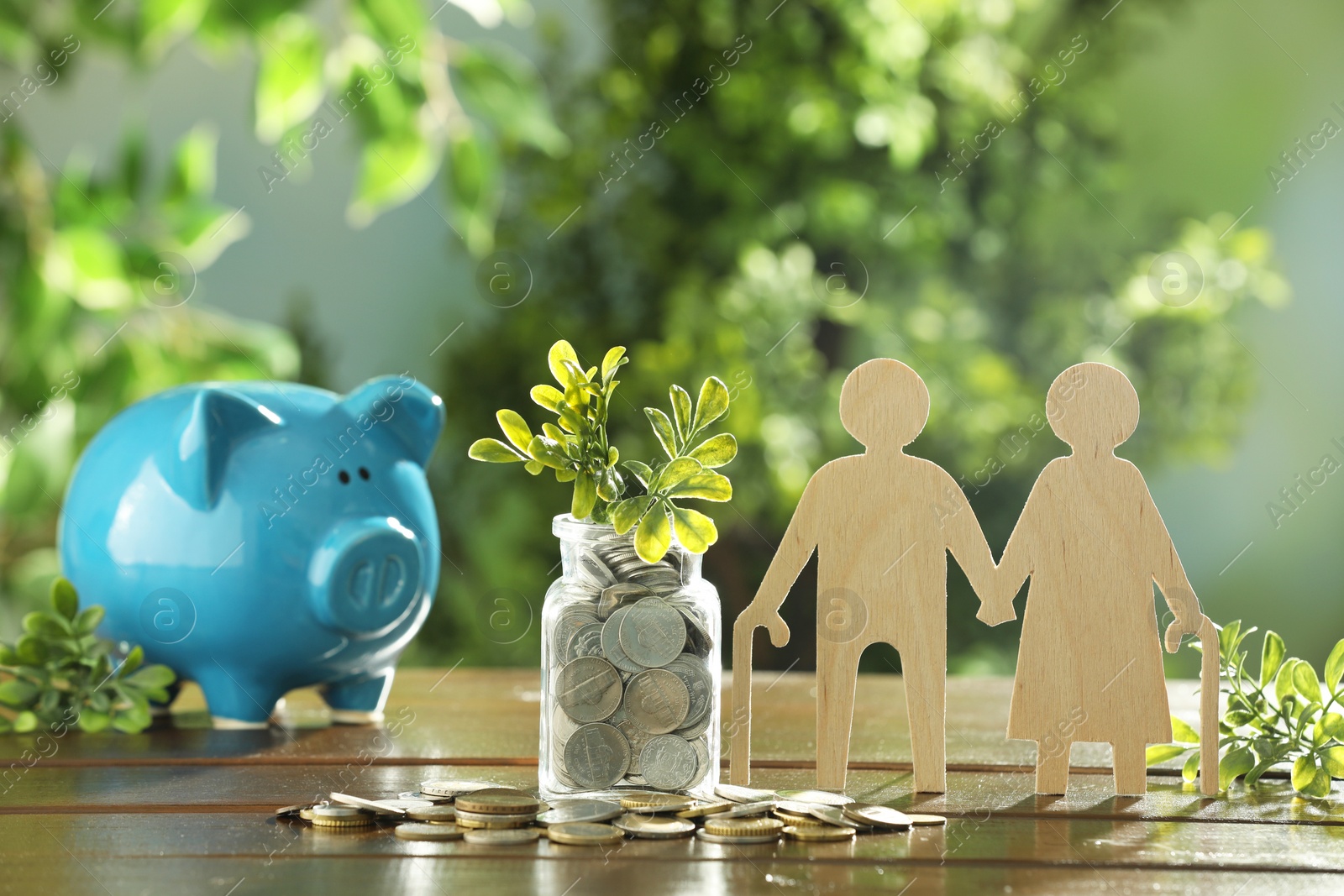 Photo of Pension savings. Figure of senior couple, piggy bank, coins and green twigs on wooden table outdoors