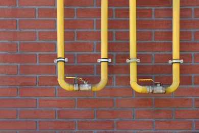 Photo of Yellow gas pipes on red brick wall outdoors