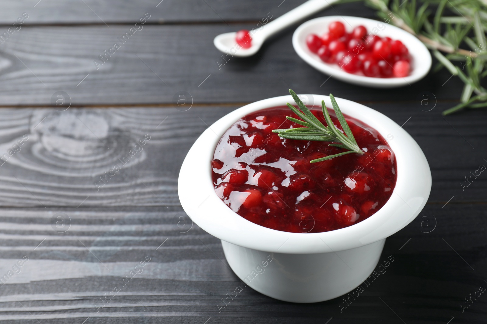 Photo of Fresh cranberry sauce in bowl and rosemary on black wooden table, closeup. Space for text