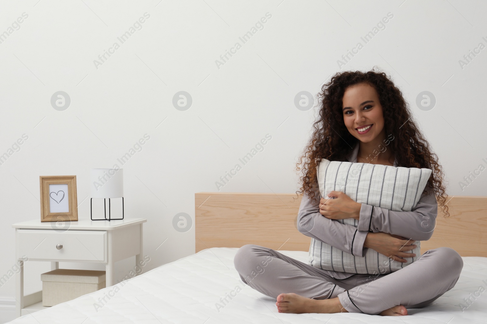 Photo of Happy young African American woman hugging pillow on bed with comfortable mattress at home