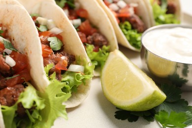 Photo of Delicious meat tacos with vegetables, lime and sauce on light table, closeup