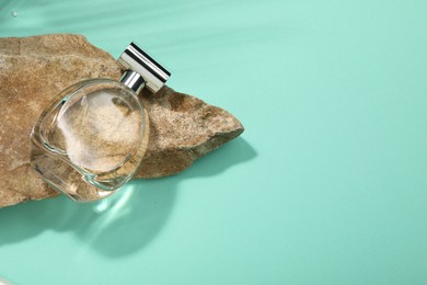 Photo of Bottle of luxury perfume in sunlight and stone on turquoise background, above view. Space for text