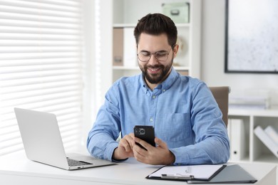 Photo of Happy young man using smartphone at white table in office