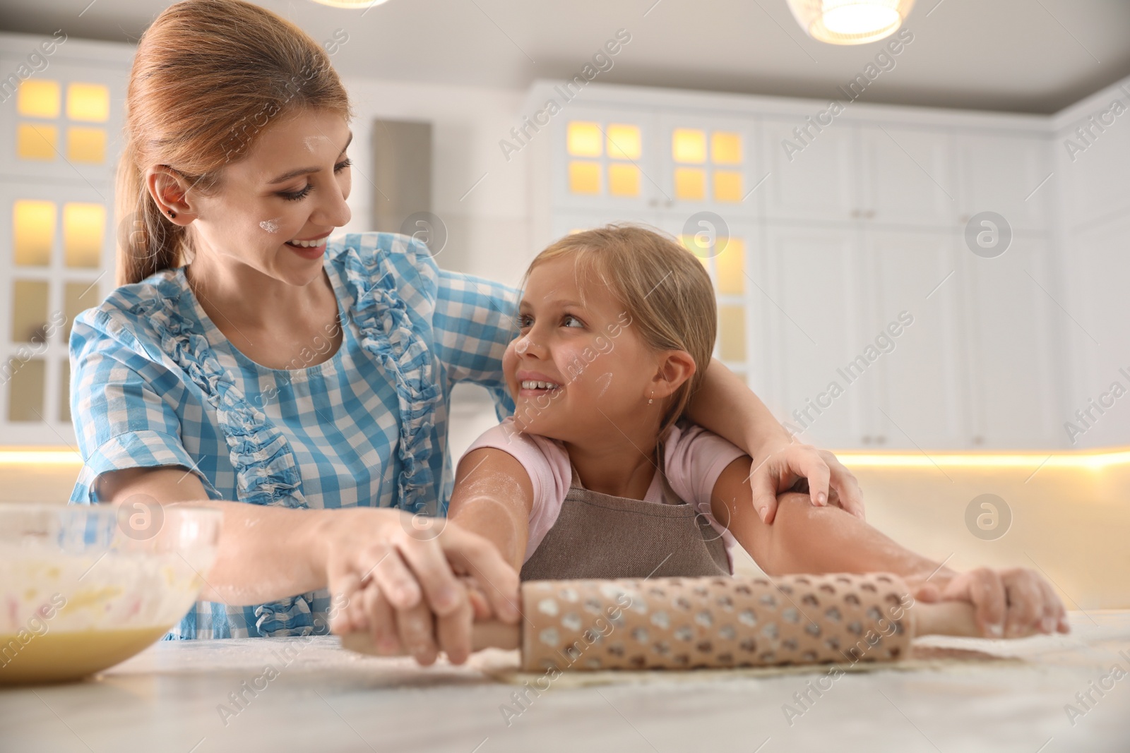 Photo of Mother and daughter rolling dough together in kitchen