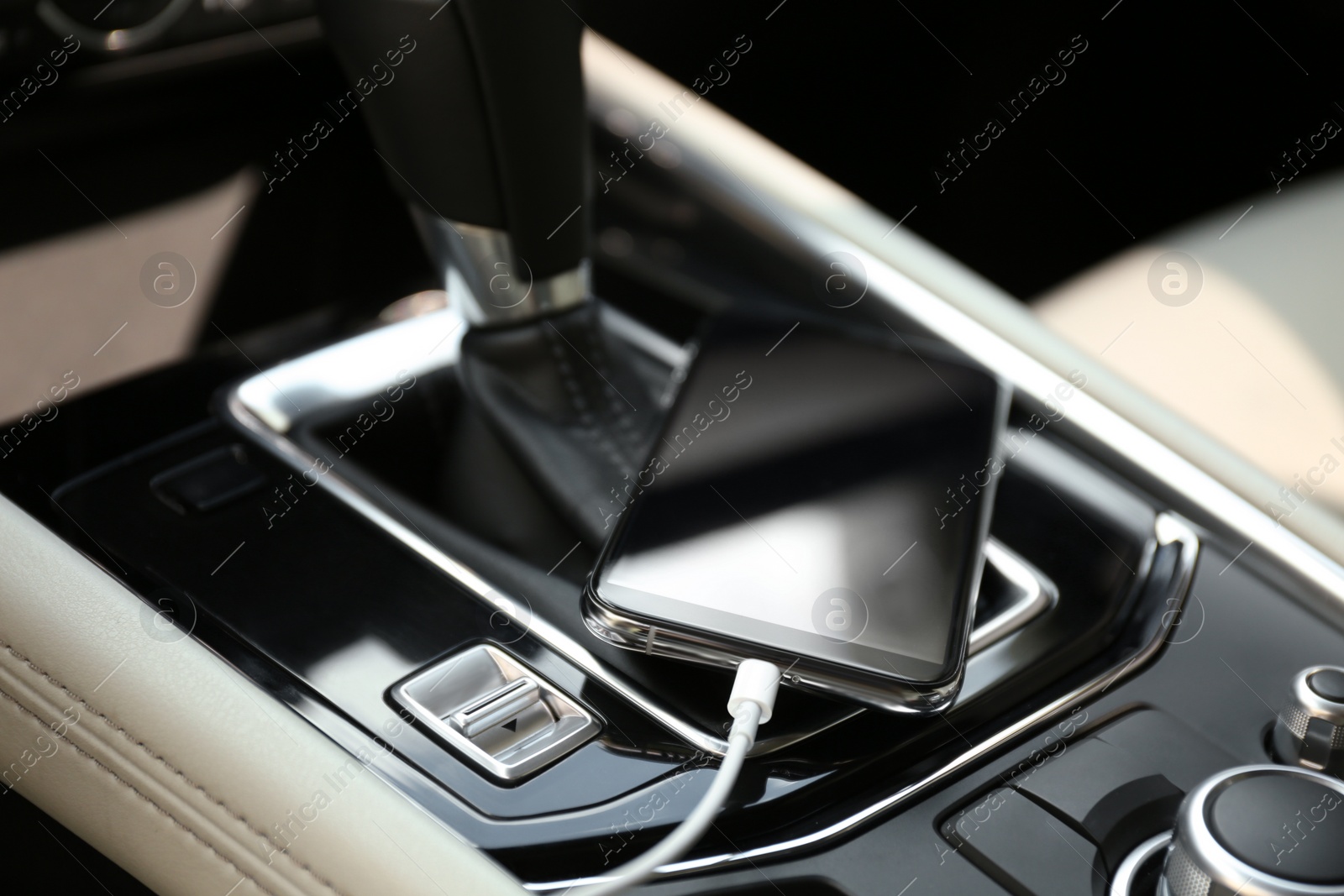 Photo of Mobile phone with charging cable in car, closeup