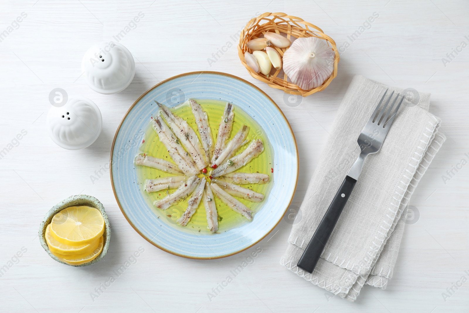 Photo of Tasty pickled anchovies with spices, garlic and lemon on white wooden table, flat lay