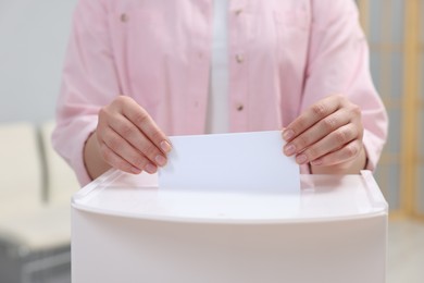 Photo of Woman putting her vote into ballot box on blurred background, closeup