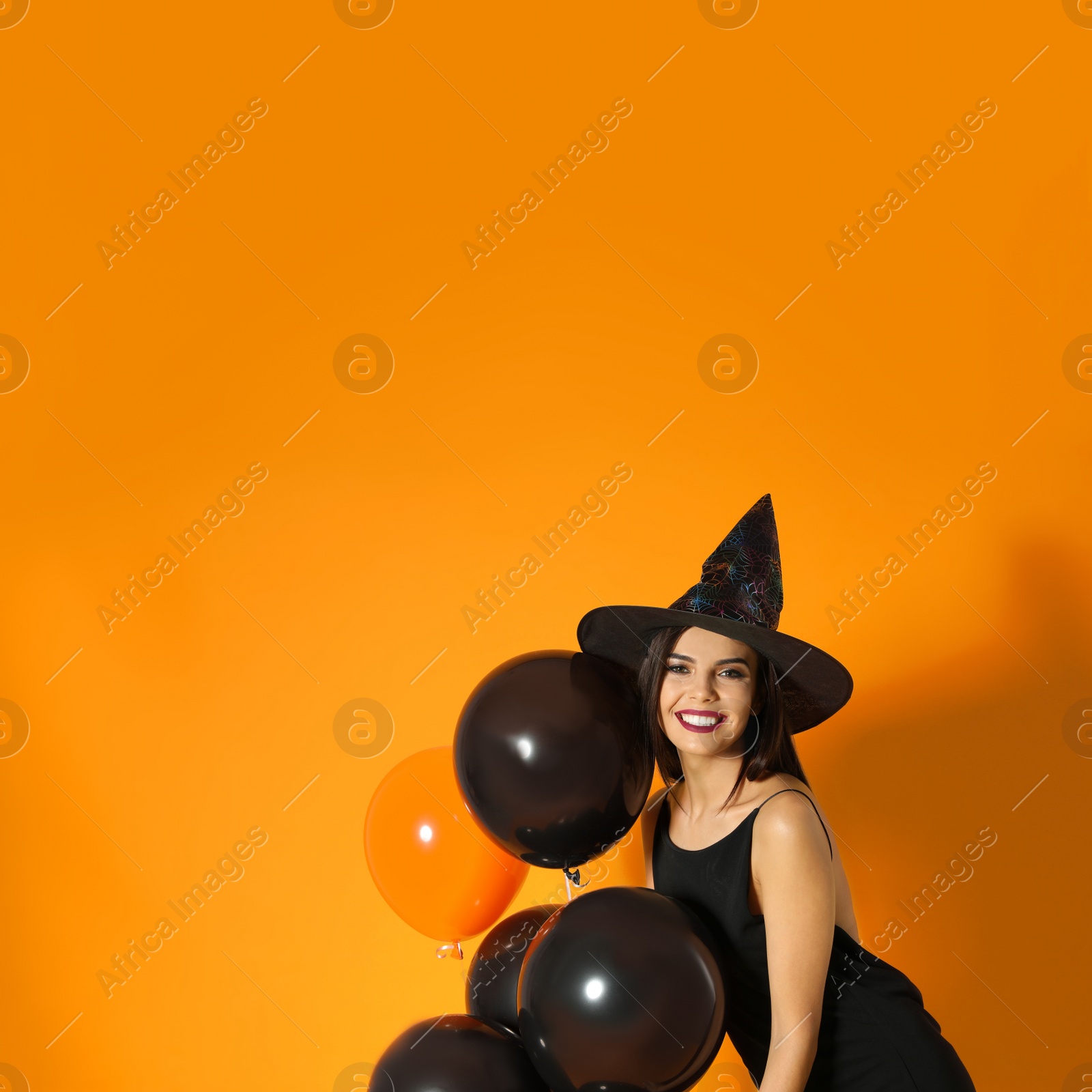 Photo of Beautiful woman wearing witch costume with balloons for Halloween party on yellow background, space for text