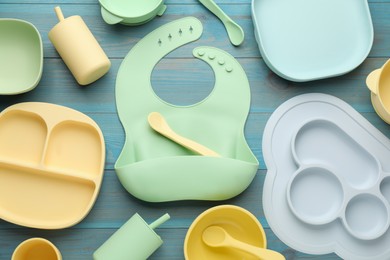 Flat lay composition with silicone baby bib and plastic dishware on light blue wooden background