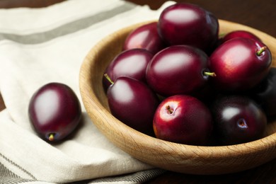 Bowl with tasty ripe plums on table, closeup