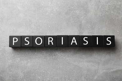 Photo of Word Psoriasis made of black wooden cubes with letters on light gray textured table, top view