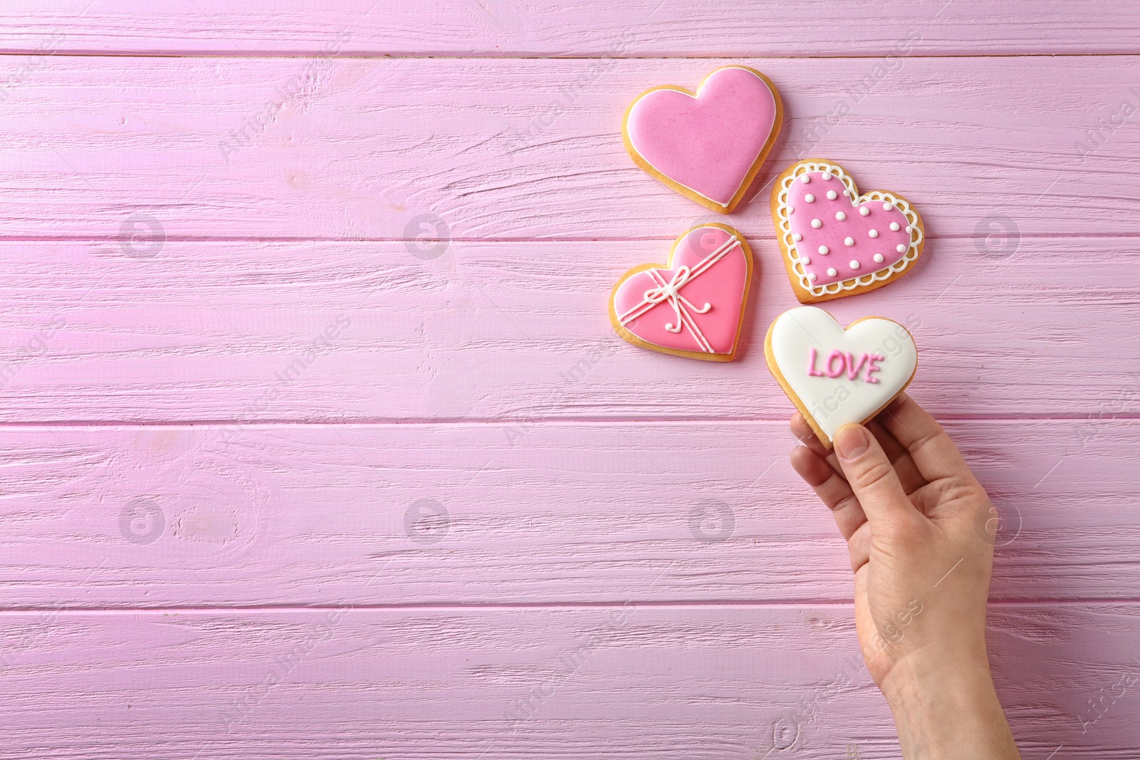 Photo of Woman holding heart shaped cookie with word Love on wooden background, top view. Space for text