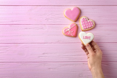 Woman holding heart shaped cookie with word Love on wooden background, top view. Space for text