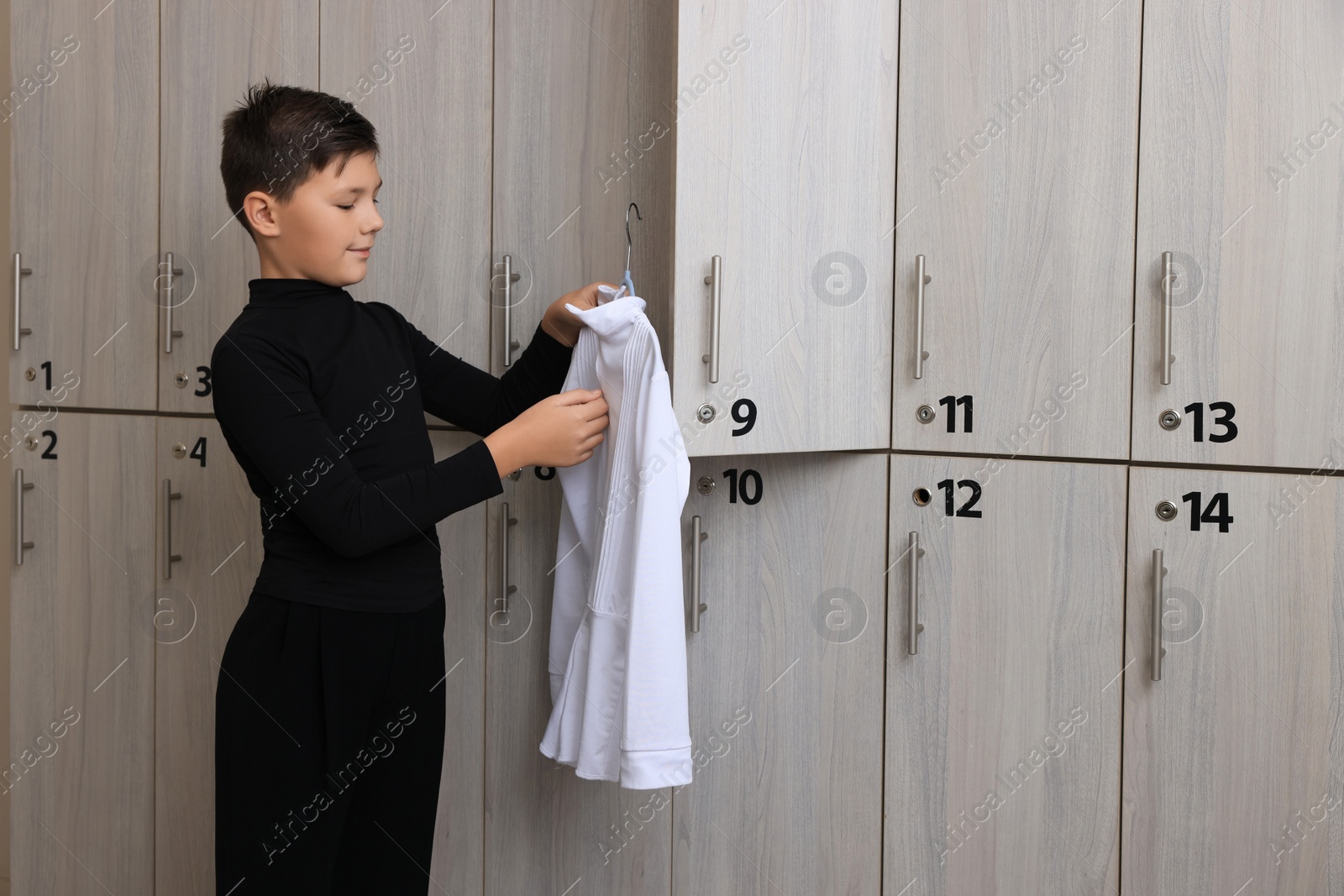 Photo of Little boy holding hanger with white shirt in locker room