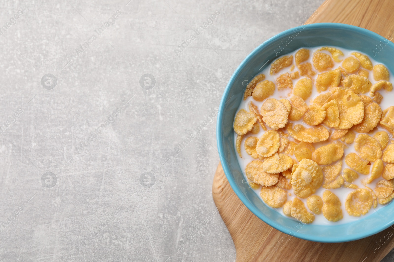 Photo of Bowl with tasty cornflakes and milk on light grey table, top view. Space for text