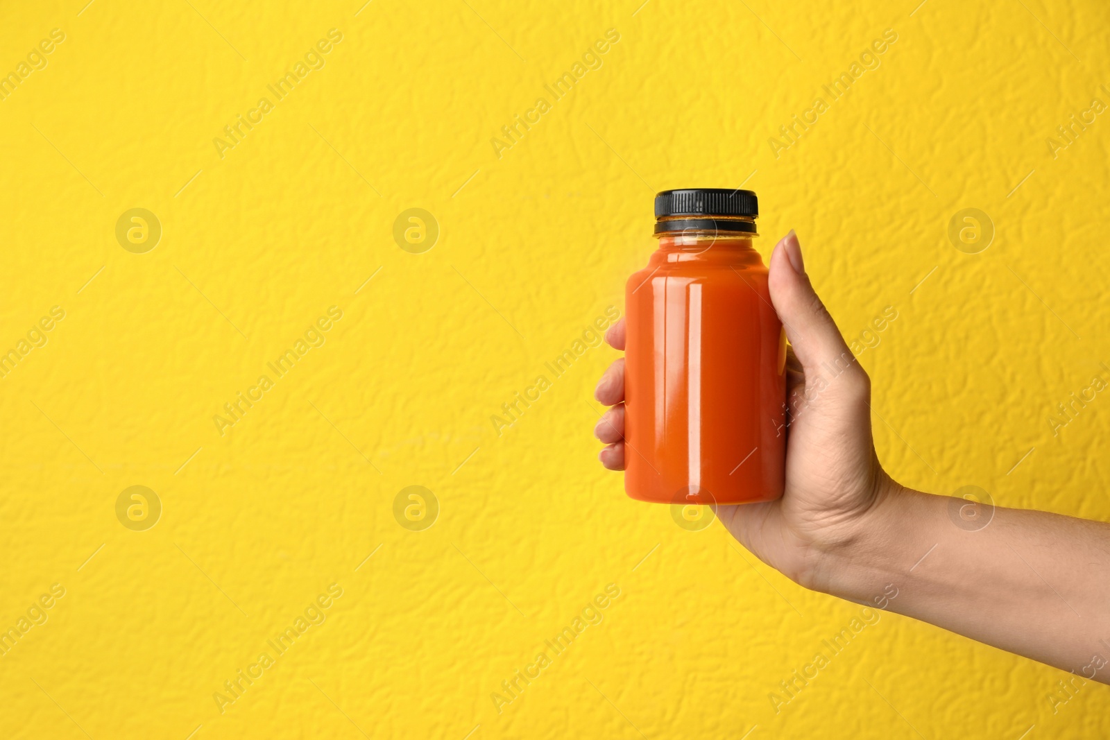 Photo of Woman holding bottle of carrot juice on color background, closeup with space for text