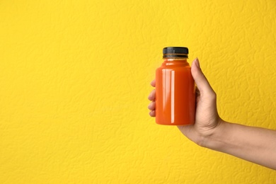 Woman holding bottle of carrot juice on color background, closeup with space for text