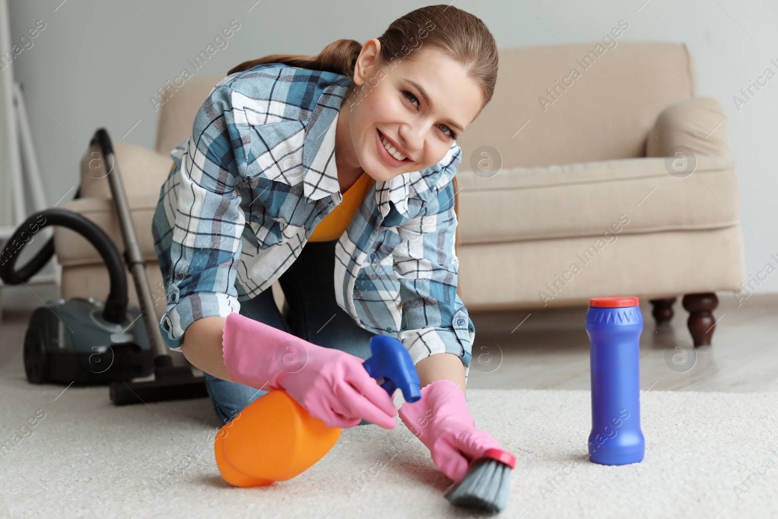 Photo of Young woman cleaning carpet at home