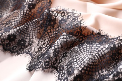 Photo of Beautiful black lace on beige fabric, closeup