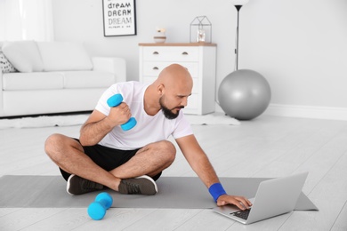 Photo of Overweight man doing exercise while watching tutorial on laptop at home