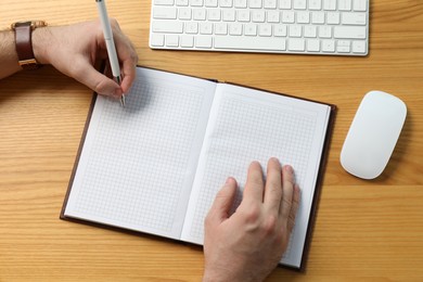Left-handed man writing in notebook at wooden desk, top view